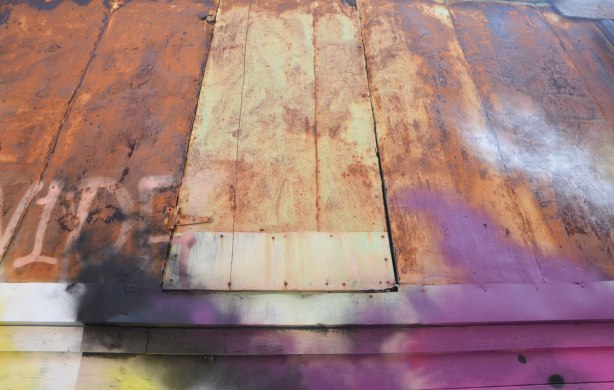 a rusty door on the upper level of an old garage in a lane, the lower level has been spray painted with street art and some of the paint is on the upper level too 