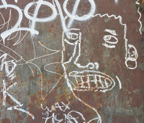white line drawing on a rusty metal door of a woman's face, slightly open mouth with lots of teeth, curly hair 