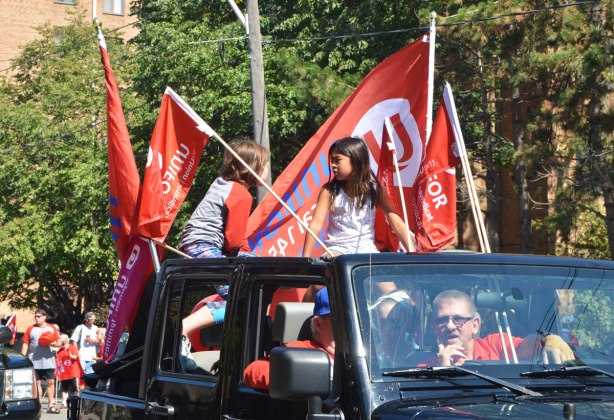 Two kids sitting in the back of a pick up truck, with red and white unifor (union) flags. Two men in the cab of the truck