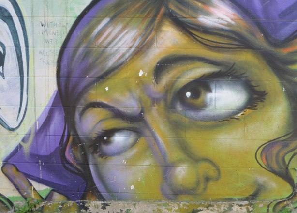 street art painting of part of a woman's face, on a wall, in greens and purples, she is looking to the left