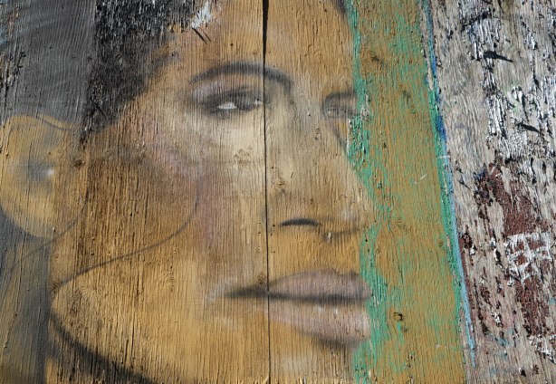 street art painting of part of a woman's face on a wooden fence, old and faded and the wood is starting to crack 