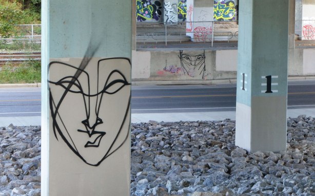 two line drawings of faces by anser on posts holding up a road