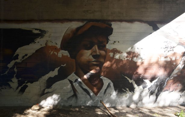 part of a mural under a bridge on the Beltline path, by StART, in brown tones of the hhistory of the railroad in the area (scenes from) a young man in a brown cap