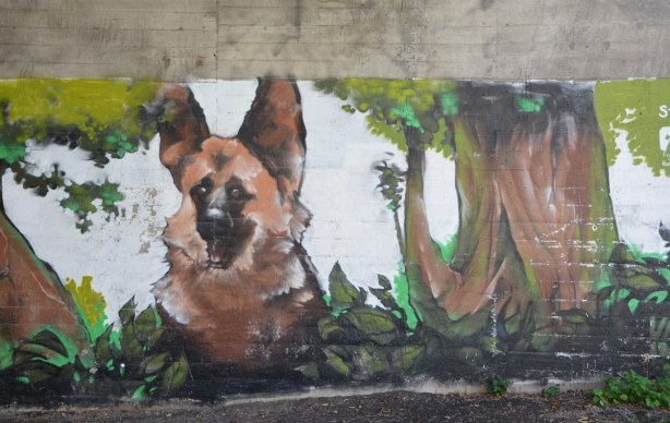 part of a mural under a bridge on the Beltline path, by StART, of nature scenes, a large dog is sitting beside a tree