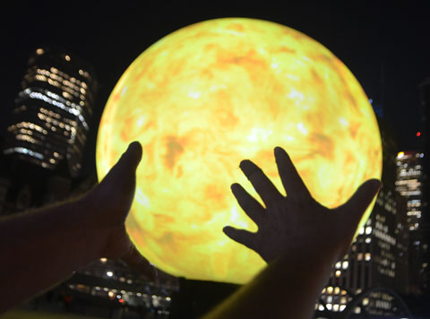 two hands silhouetted on a large yellow globe representing the sun, night time.
