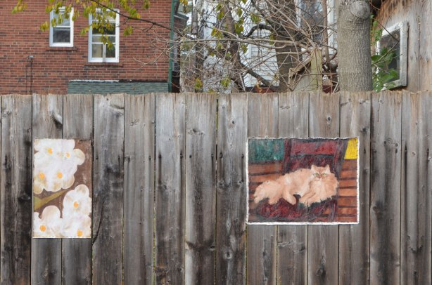 two painting on a fence. One is of a cat and the other is of white flowers