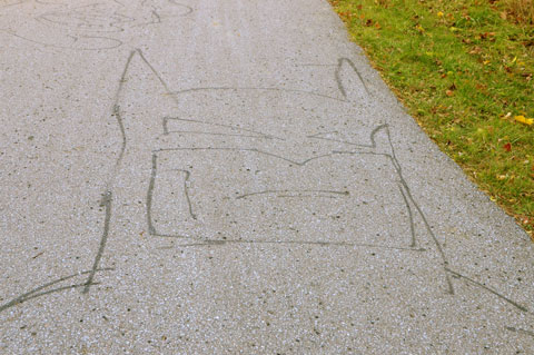 line drawing in black of Batman's head and shoulders, drawn on a paved path in a park 