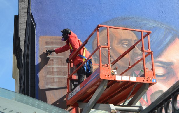 elicser painting a large mural by CP 24 parkinglot on Queen St West, showing people in the tv business - up close picture of him with a can of spray paint in his hand. 