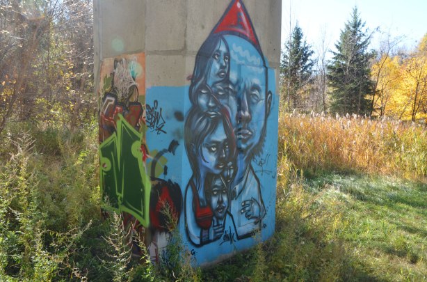 street art by elicser in blue of a family. Man with red hat, woman and kids huddled together, fall park scenery in the background.