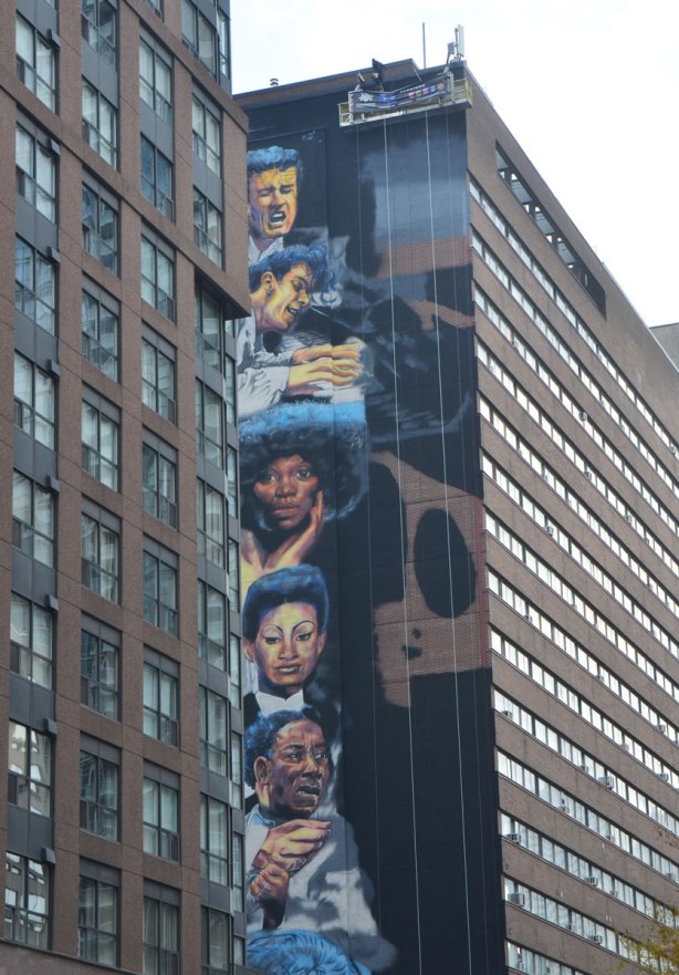 a vertical mural painted on the side of a multi storey building, the mural is a series of faces. 