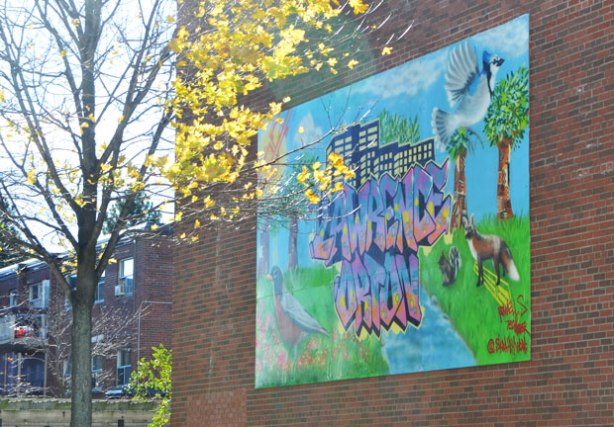 a mural on the side of a building that has the words Lawrence Orton in blue and orange. There is also a blue jay in flught, a fox and a squirrel and a robin standing in the grass.