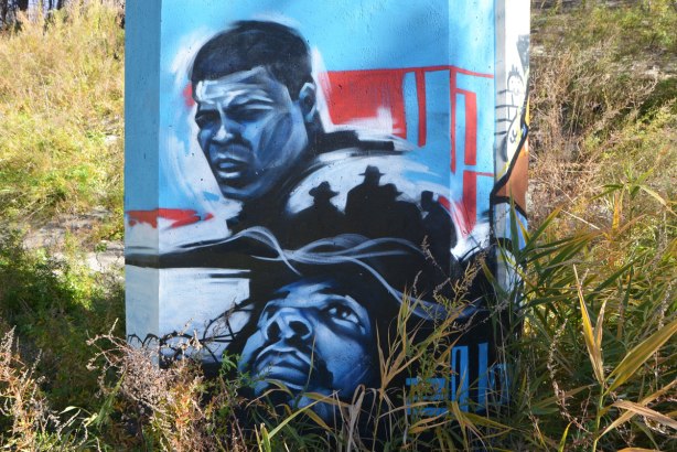 street art on the bottom of a concrete pillar, two black men. One is Mohammad Ali. 
