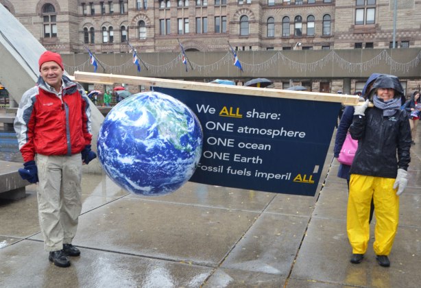 people at a rally protesting against Donald Trump as President of the USA, two people holding a banner with a 3D model of the earth with a sign that says We all share one atmosphere, one ocean , one earth, fossil fuels imperil all