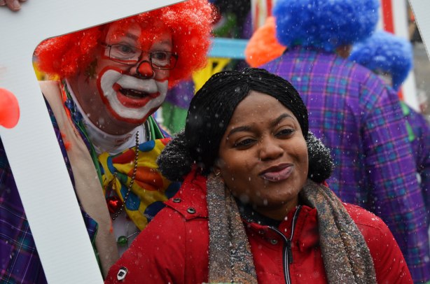 Santa Claus Parade - a black woman in a red jacket and brown scarf poses with a man in a clown costume with bright red hair. 