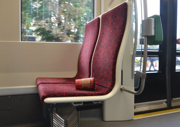 an empty red tim hortons coffee cup lies on a red TTC streetcar seat. No one is sitting there. 