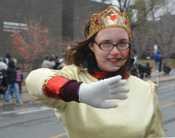 Santa Claus Parade - a young woman with a gold crown decorated with little red hearts, wearing a pale yellow dress, walking in the parade, waves at the camera 