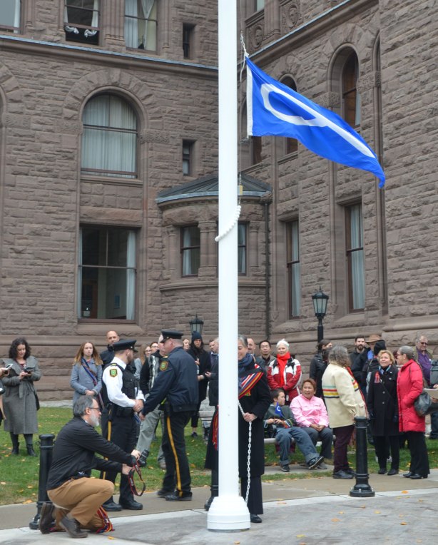 raising a blue Metis flag in front of Queens Park