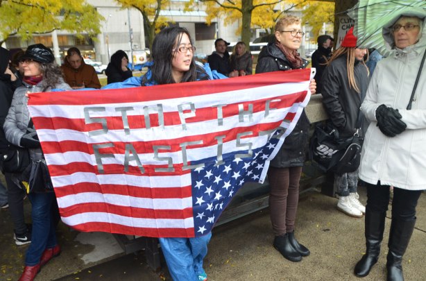 a woman holds the American flag upside down. The words stop the fascists have been added to the flag with tape . a protest rally at Nathan Phillips Square on a rainy day