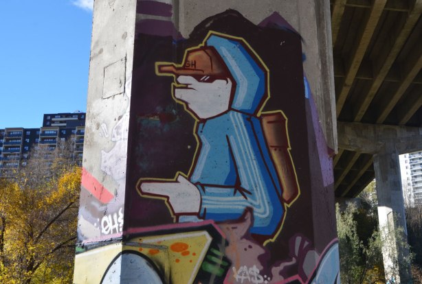street art painting on a pillar under a bridge of a young man in a blue hoodie and brown baseball cap