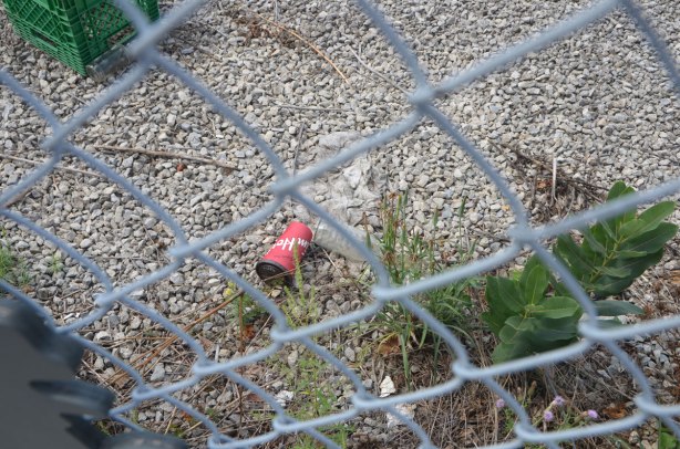 a tim hortons cup discarded onto a gravel section of a vacant lot, behind a chainlink fence