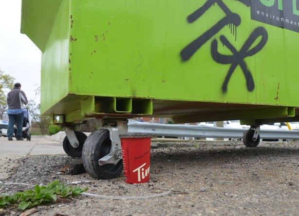 a red tim hortons cup standing on the ground beside a green rubbish bin 