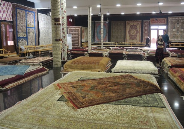 The inside a carpet showroom in Bukhara with many carpets of different sizes stack on the floor and hanging on the walls. Almost all the walls are covered. 