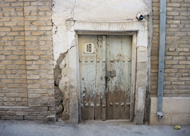 an old wood door with peeling light turquoise paint, on an old stone building, with the number 18 on the door. 