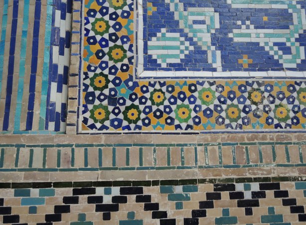 detail of patterns of rectangles and pentagon and hexagon shaped tiles in blue, yellow, black and white, on the front of a madrasah in bukhara 