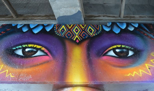 pillars and supports under an overpass that have been painted in bright colours by smoky and shalak - a face showing eyes and top of nose