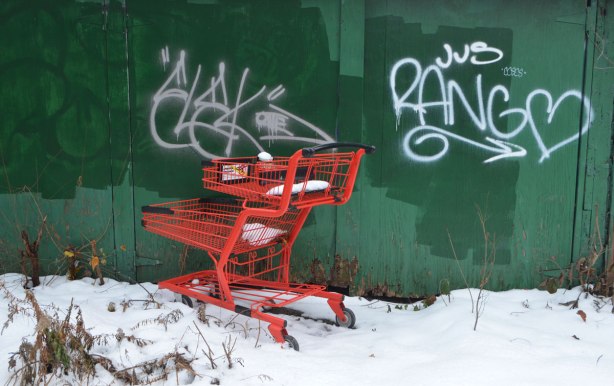 a bright red shopping cart has been abandoned in front of a green garage door in a snowy alley