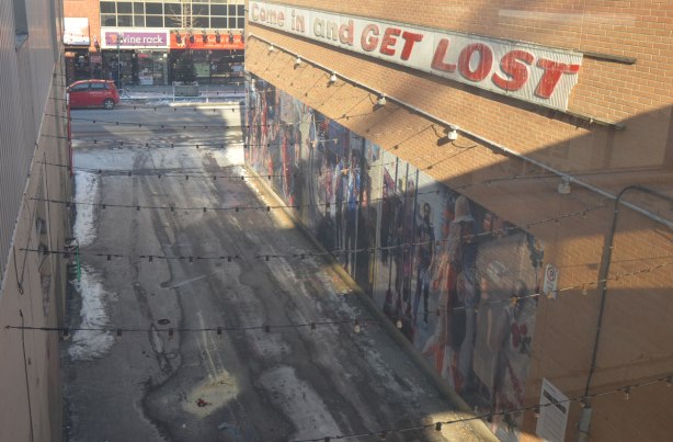looking down on an alley, there is a mural along the side of one of the buildings. 