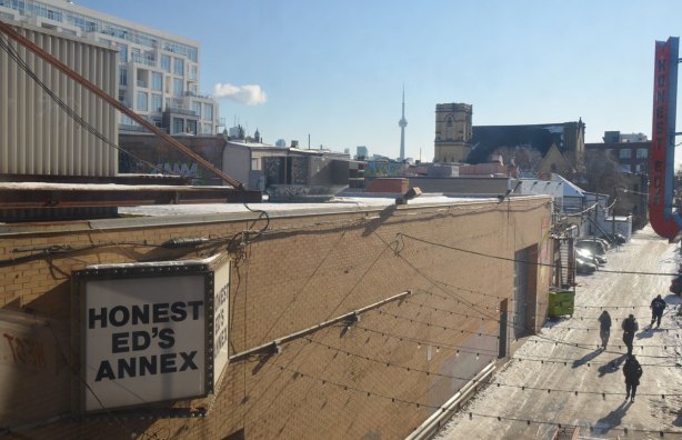 looking down at an icy alley where four people are walking between buildings, sign on building says Honest Eds Annex, 