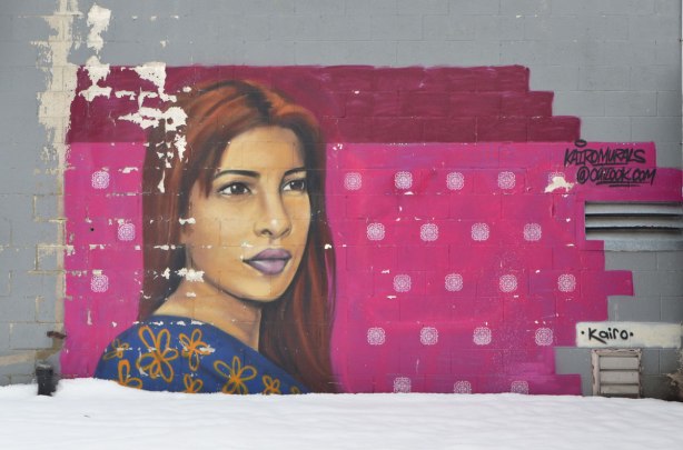mural of a woman's head by kairo. Background has been painted a dark pink, with white spots. WOman has long reddish brown hair. 