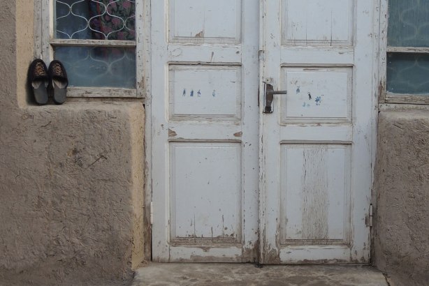 closed white double doors with small windows on either side, a pair of shoes neatly sitting by the window. 