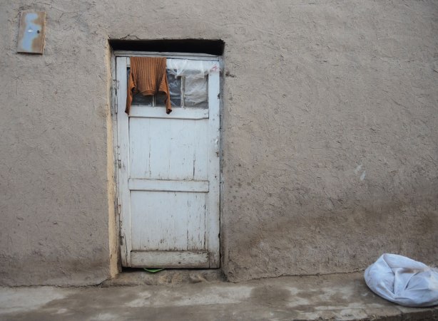 a brown sweater is hanging over the top of an old white door on a mud and straw house 
