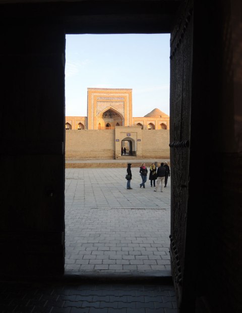 view through a doorway to a courtyard in front of a mosque, with a group of people standing there 