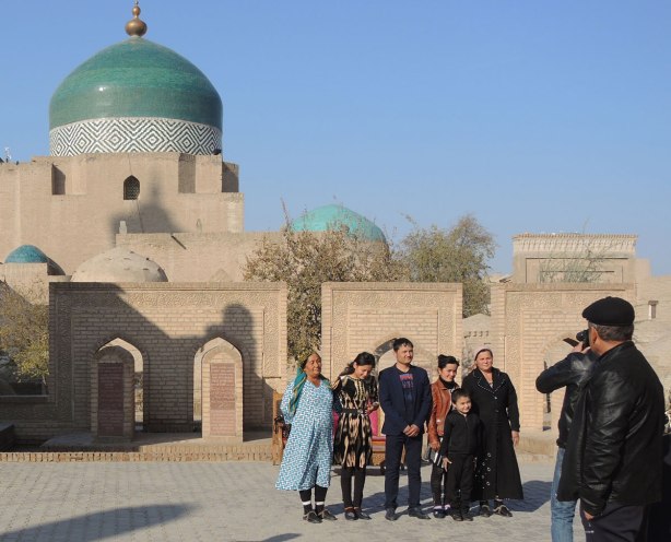 local Uzbeks (probably) lining up in front an old brick building with a blue dome to have their picture taken