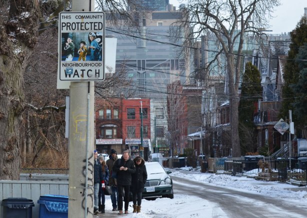looking down a street in Kensington, looking towards Spadina, older brick housses on the street, a group of people walking down the sidewalk, snow on the ground, winter trees, a neighbourhood watch sign that has been altered with a picture of the three boys from the movie 3 Ninjas.