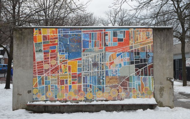 a mural on a conrete wall in a schoolyard that is a map of the area with the school in the center, colourful, about 8 feet high and twelve feet wide. 