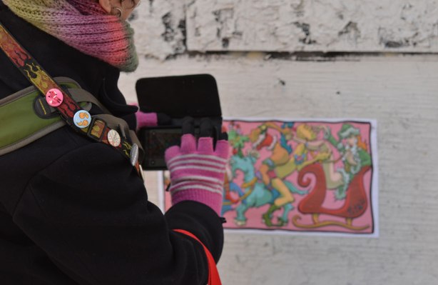 a woman in pink gloves is taking a picture of a graffiti paste up in a street, taking the photo with her phone