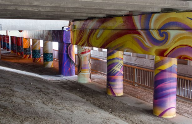 pillars and supports under an overpass that have been painted in bright colours by smoky and shalak - swirls of purples and yellows