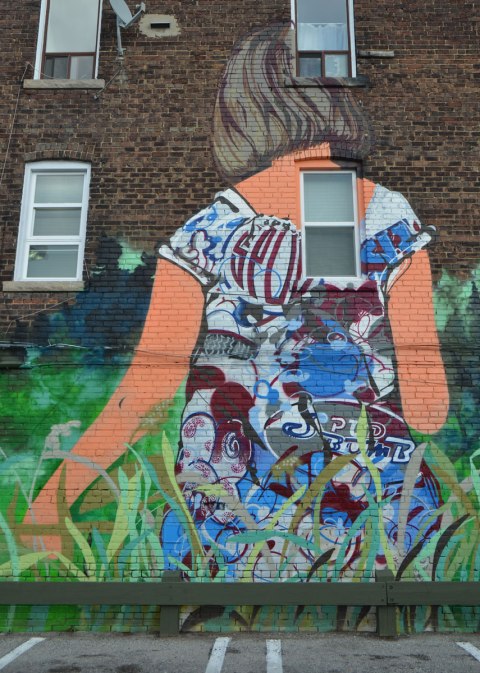 part of a larger mural, a young woman with her back to the viewer, walking through long grass 
