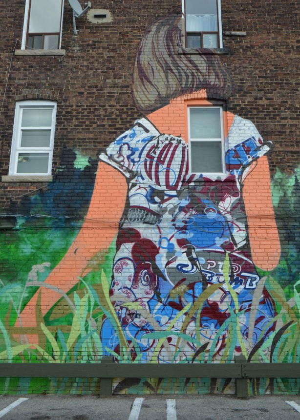 part of a larger mural, a young woman with her back to the viewer, walking through long grass 