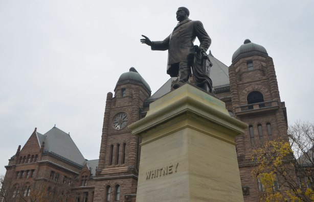 statue of a mna with his right arm extended, Whitney, in front of the parliament buildings at Queens Park. 