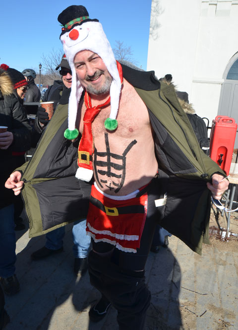 people participating in the 12th annual polar bear dip at Sunnyside Park in Toronto, in the icy cold water of Lake Ontario - a swimmer with a Santa outfit sort of, apron and tie