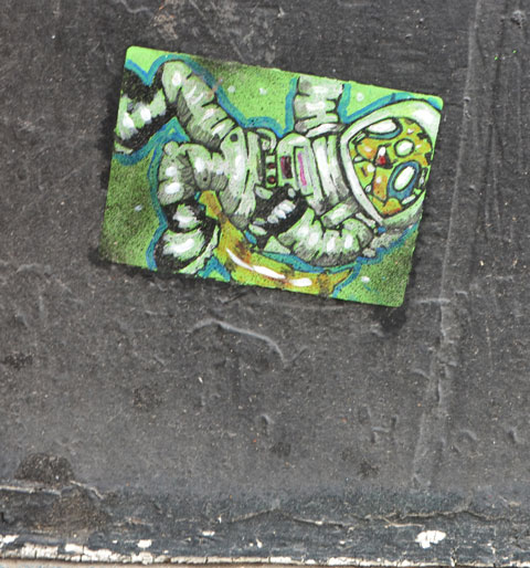 a small paste up of an astronaut floating in space, on a black wall, close to the ground.