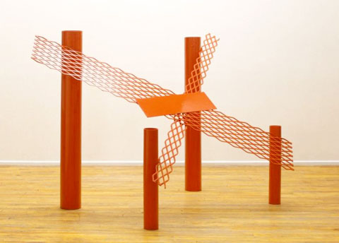 red sculpture by anthony caro, metal, 4 upright cylindrical tubes with metal mesh forming an X on top of them.