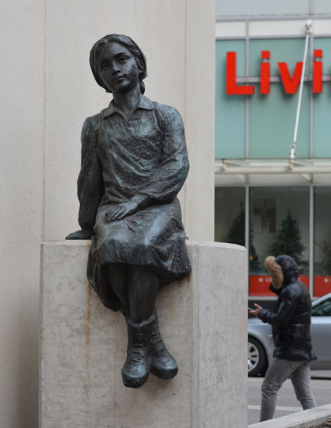 sculpture, Two Children of Toronto by Ken Lum in a downtownwalkway with a concrete bulding beside it, looking towards the girl, with Bay Street and Canadian Tire store behind 