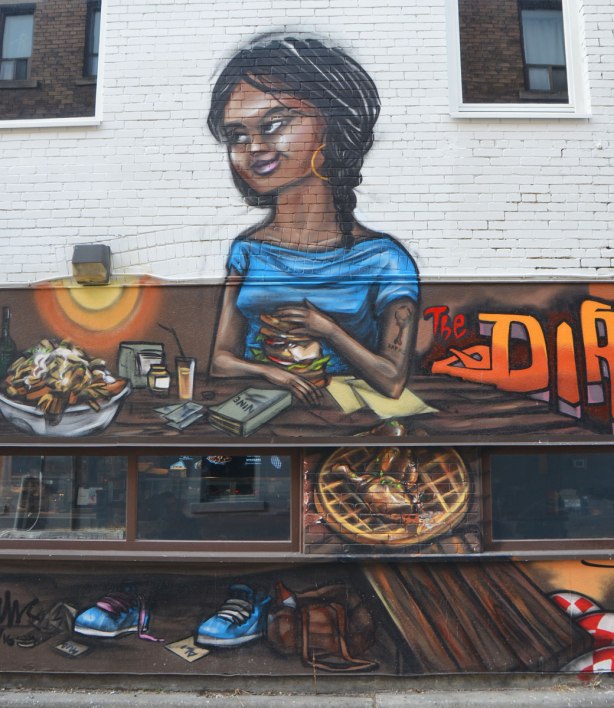 from a mural by elicser along the exterior wall of the dirty bird chicken and waffle restaurant - a woman is sitting at a table in the restaurant
