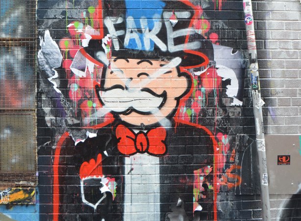 the man from the monopoly game is painted on a wall. Someone has sprayed a white x through his face and written the word fake on his top hat.
